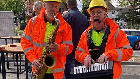 Muzikanten gekleed in wegwerkersjassen spelen op een saxofoon en keyboard