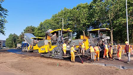 Werkmannen staan bij de machine die het nieuwe asfalt stort